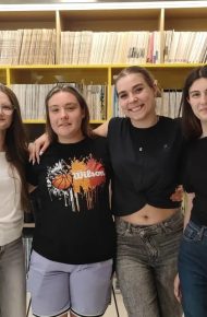 Cinque studentesse e studenti sorridenti in posa davanti agli scaffali di libri della mediateca, accanto a una delle fotografie esposte.