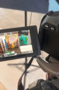 Lo schermo di una fotocamera su treppiede inquadra alcuni libri illustrati e un libro a fisarmonica colorato esposti su un tavolo.