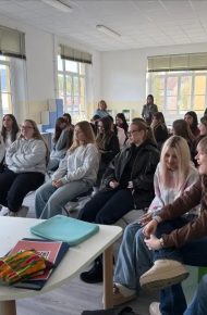 Studentesse e studenti seduti in un’aula luminosa seguono il laboratorio; in primo piano un tavolo con un computer portatile aperto, alcuni docenti in piedi sul fondo.